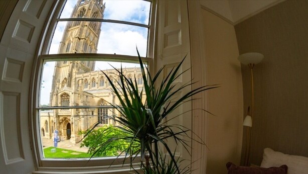 A room with a large window, a potted plant, and a lamp. - Church Lane Apartments (Boston)