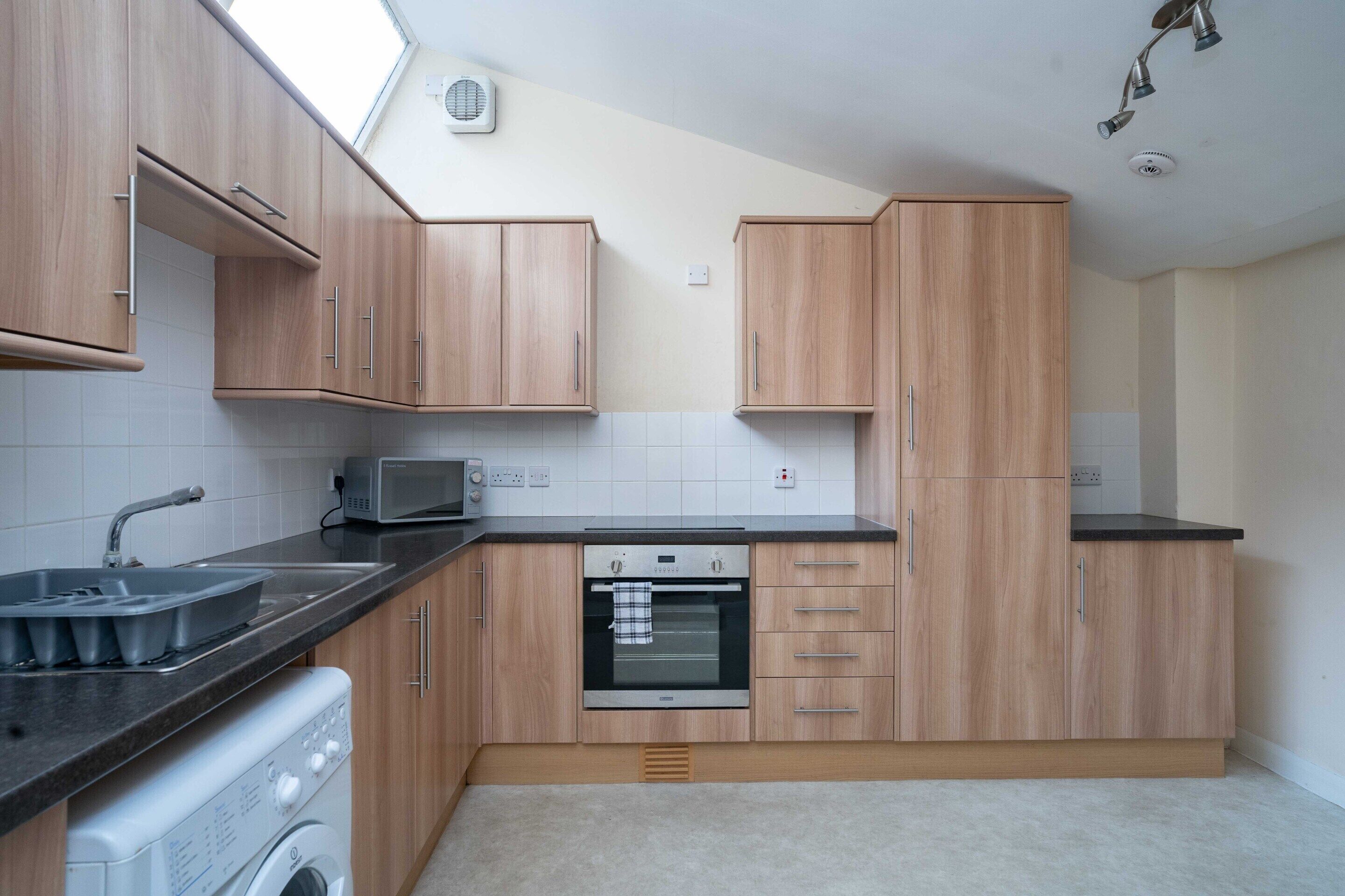 Una cocina con armarios de madera, microondas, horno y lavadora.