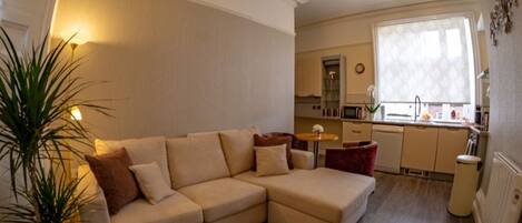 A modern living room with a beige sectional sofa, a small round table, and a potted plant.