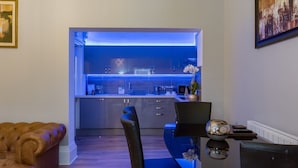 A modern kitchen with blue under-cabinet lighting, a dining area with a black table and chairs, and a brown leather sofa. - Church Lane Apartments (Boston)