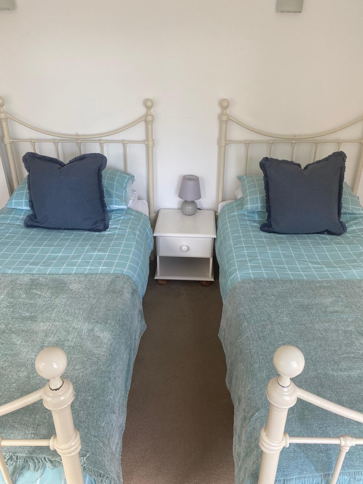 Habitación doble con dos camas, cada una con cabecero y almohada, una mesita de noche con lámpara y un cajón pequeño.
