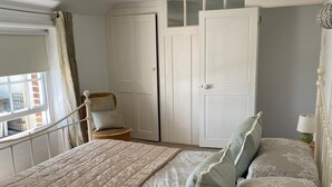 Une chambre à coucher avec un grand lit, une chaise, une armoire et une fenêtre avec des rideaux.
