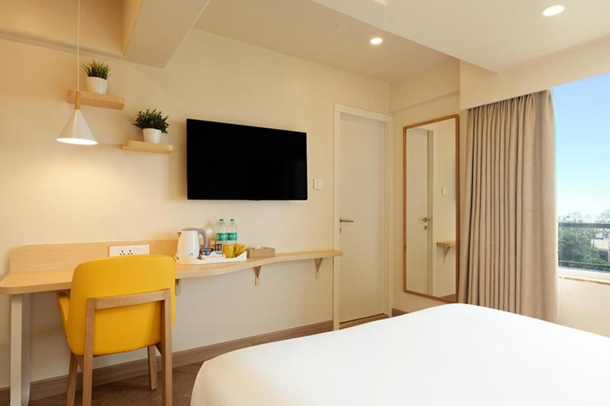A hotel room with a bed, a desk with a chair, a television, and a window with curtains.