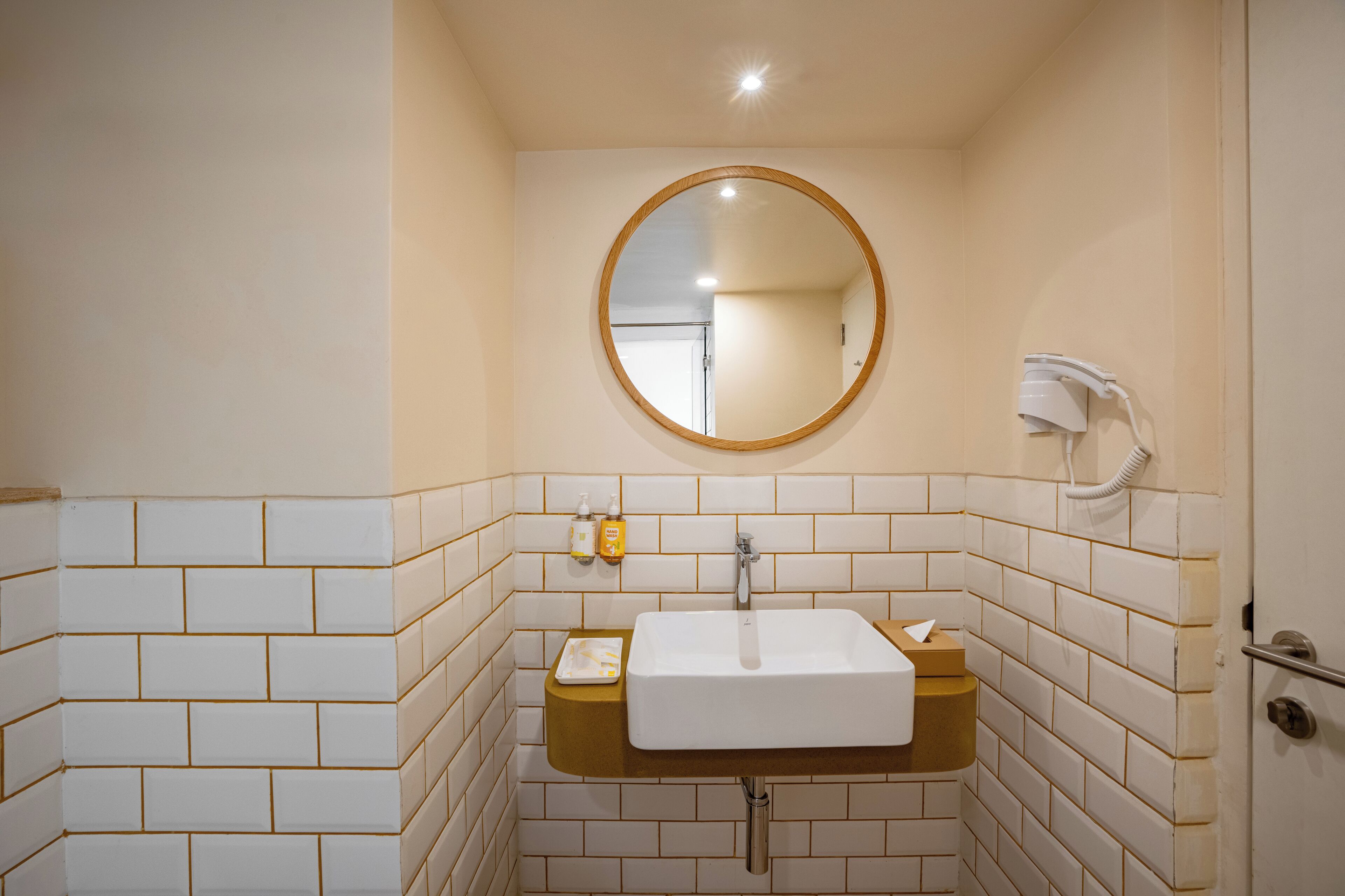 A bathroom with a white sink, a round mirror, and a hand dryer.