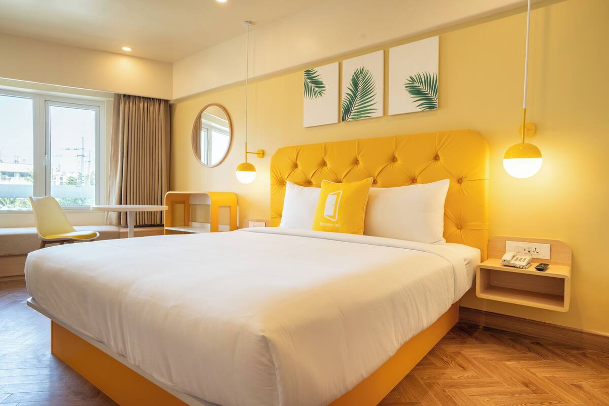 A large bed with white bedding, a yellow headboard, and a bedside table with a phone and a lamp.