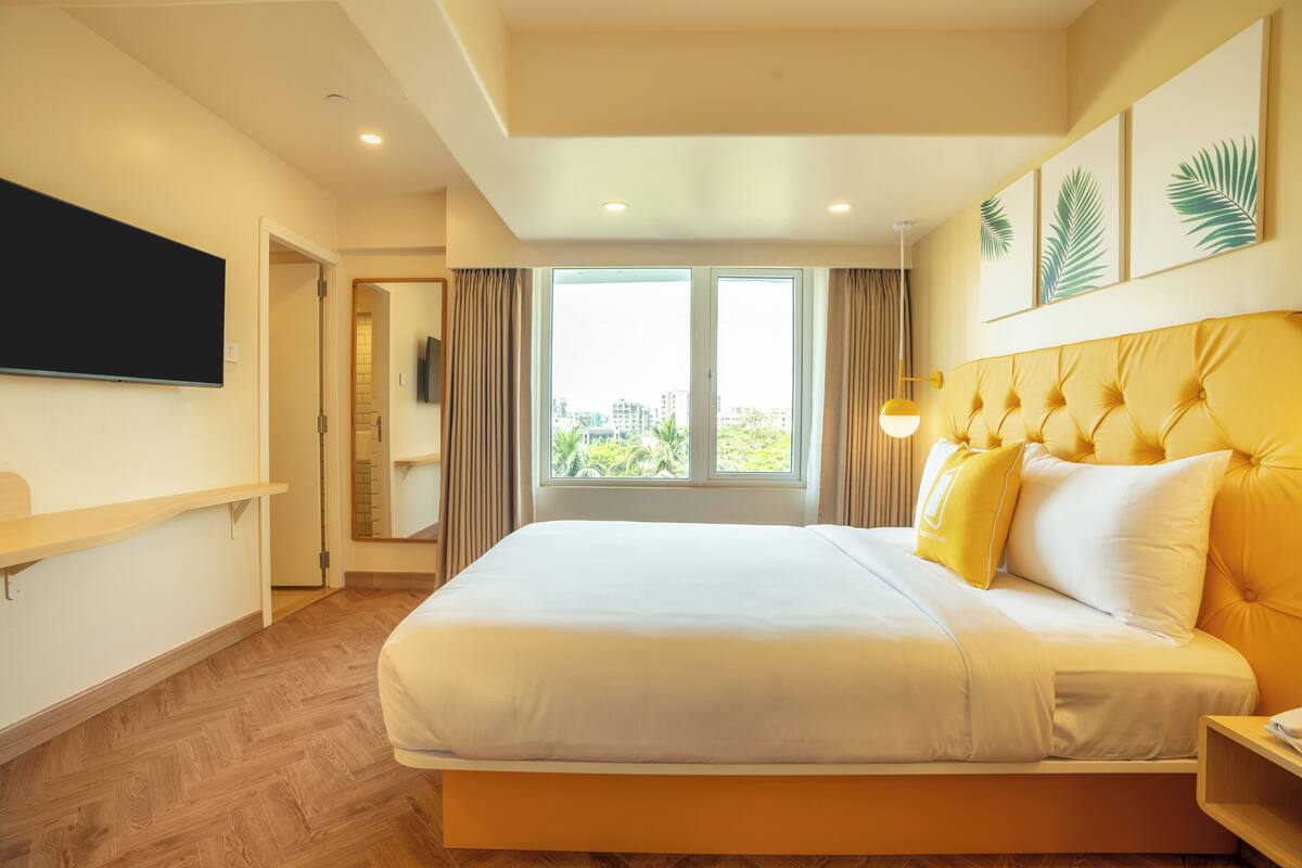 A modern hotel room with a large bed, a flat-screen TV, and a city view.