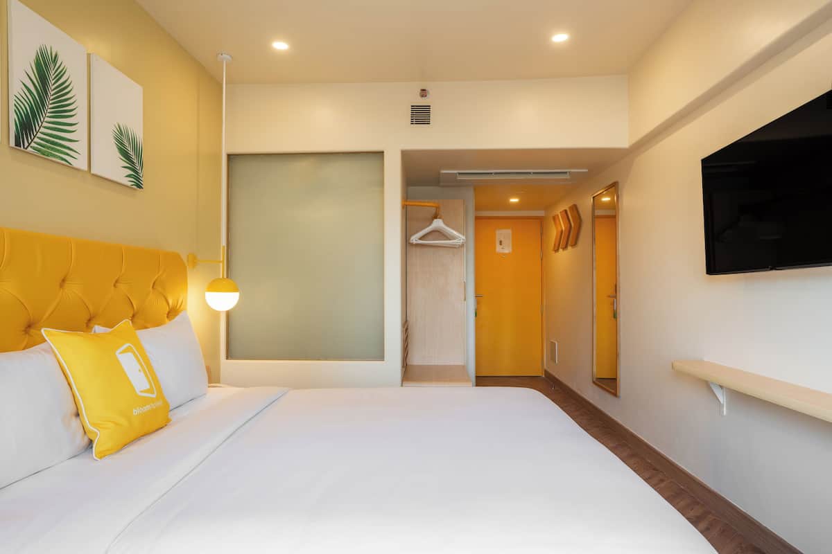 A hotel room with a bed, a TV mounted on the wall, and a hallway leading to a bathroom.