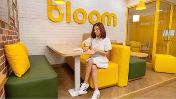 A person sitting at a table in a room with yellow and green furniture, a brick wall, and a 'bloom' sign on the wall.