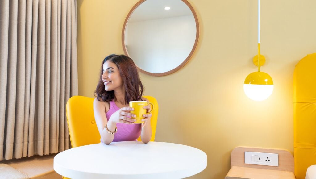 Una habitación con una mesa redonda, una silla amarilla, una lámpara amarilla y un espejo en la pared.