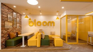 A modern interior with a brick wall, yellow furniture, and a 'bloom' sign. - Bloom Hub WEH Andheri (Mumbai)