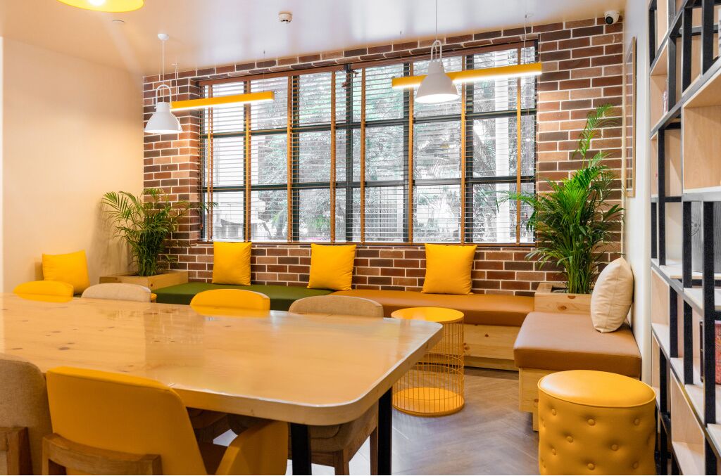 Un intérieur moderne avec un mur en briques, de grandes fenêtres, des sièges jaunes et une table en bois.