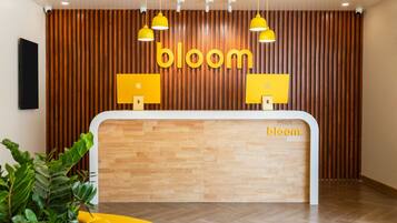 Vastaanottotiski, jonka yläpuolisessa seinässä ja katossa on sana ”bloom”, puupanelointi ja keltaiset riippuvalaisimet.