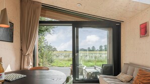A modern room with a wooden ceiling, a glass door leading to an outdoor area, a sofa with a tiger print pillow, and a table with chairs.