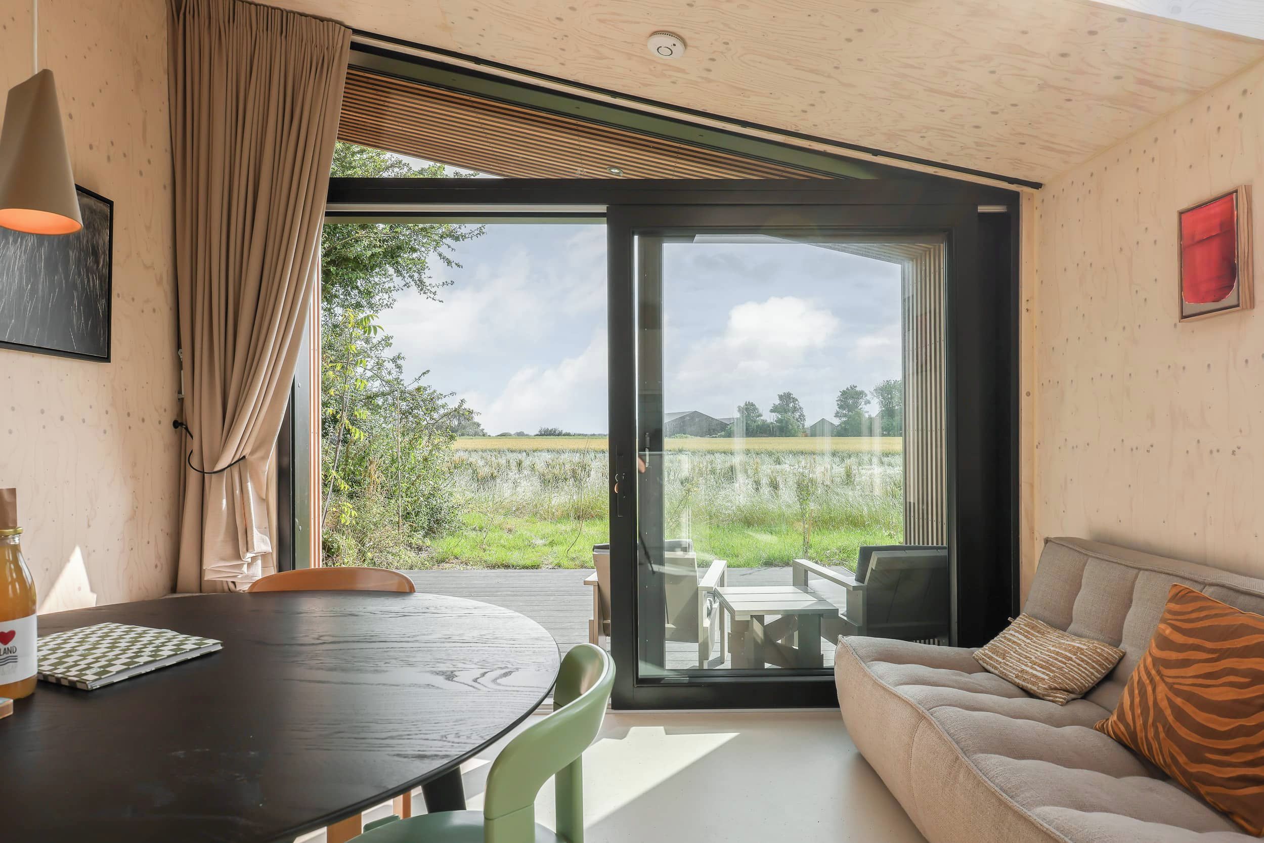 A modern room with a wooden ceiling, a glass door leading to an outdoor area, a sofa with a tiger print pillow, and a table with chairs.
