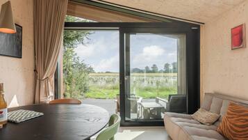 A modern room with a wooden ceiling, a glass door leading to an outdoor area, a sofa with a tiger print pillow, and a table with chairs.