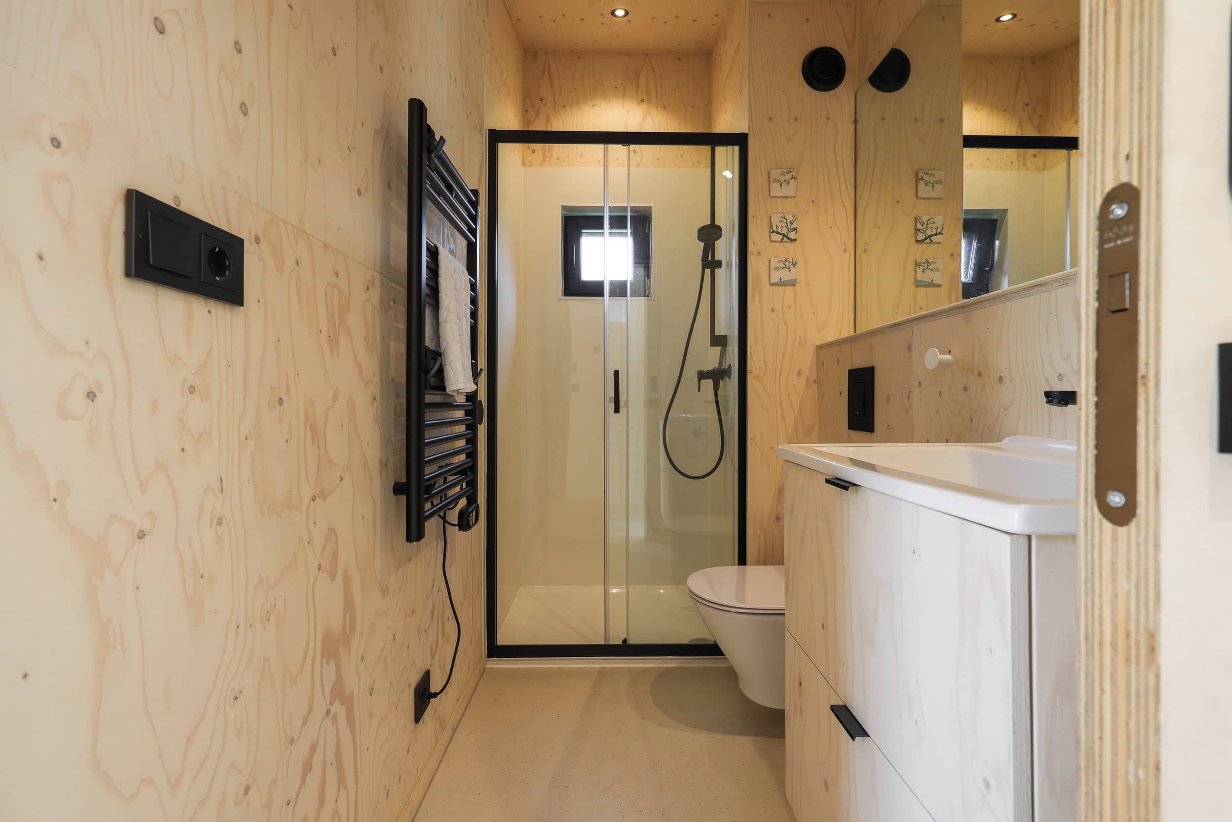 Une salle de bain moderne avec une douche à parois de verre, des toilettes blanches et un meuble-lavabo en bois avec un miroir.