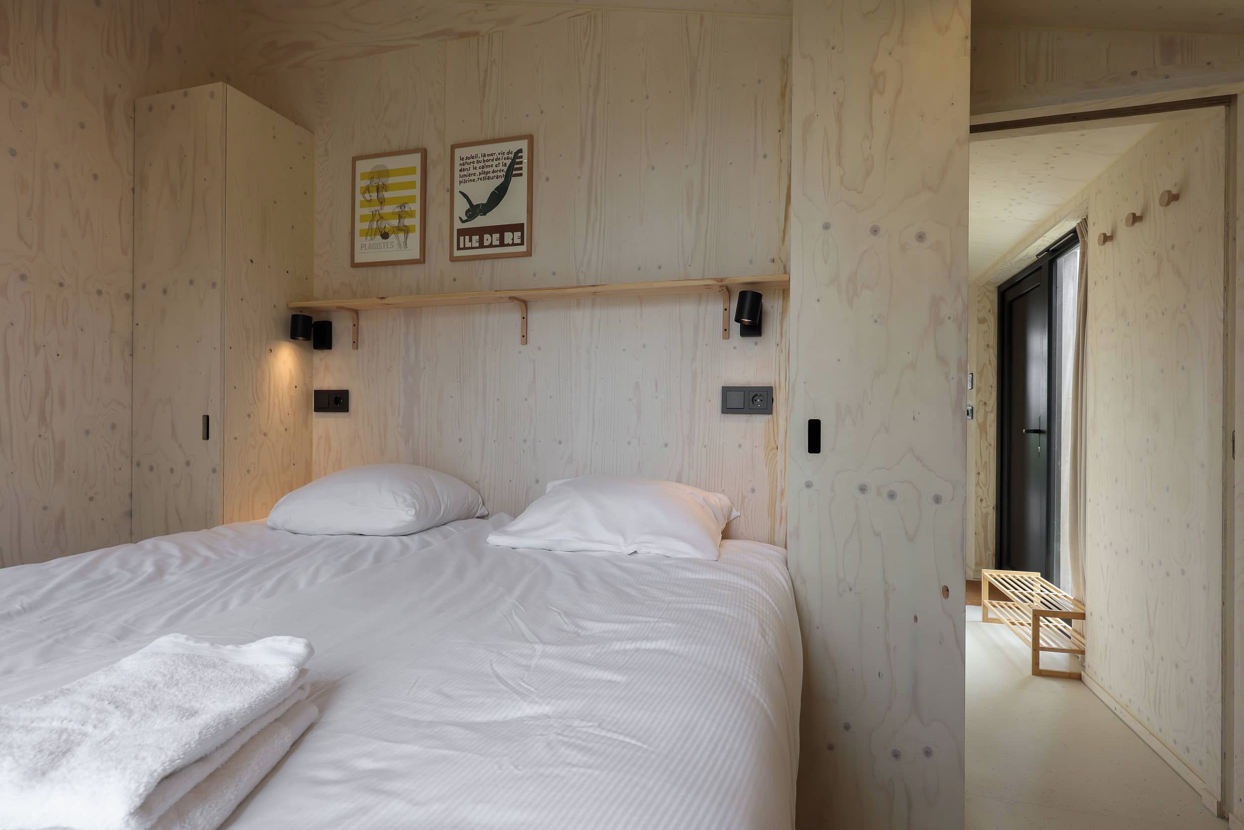 A wooden-paneled bedroom with a bed, two wall-mounted light fixtures, and a framed poster.