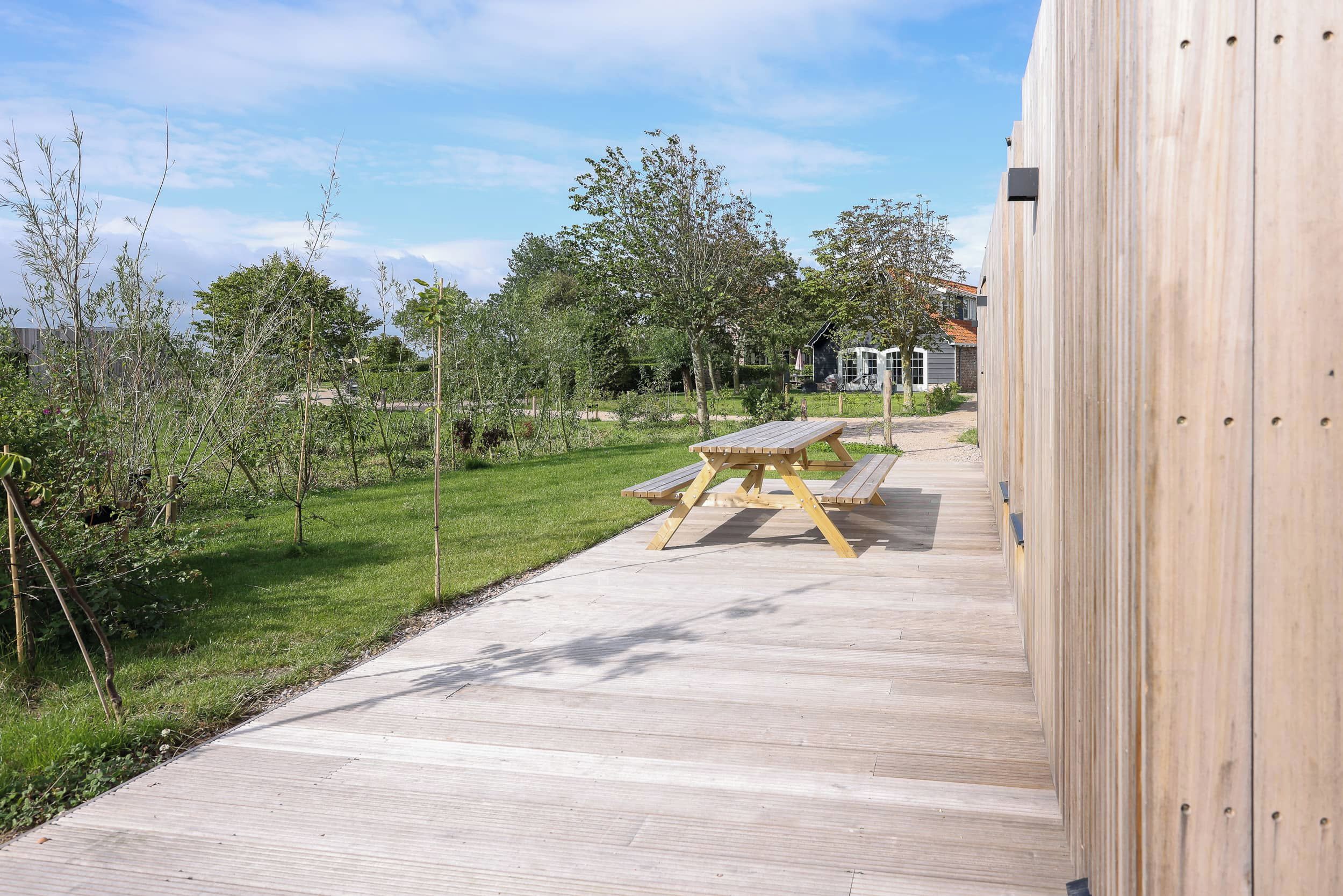 A wooden deck with a picnic table, surrounded by greenery and a house in the background.