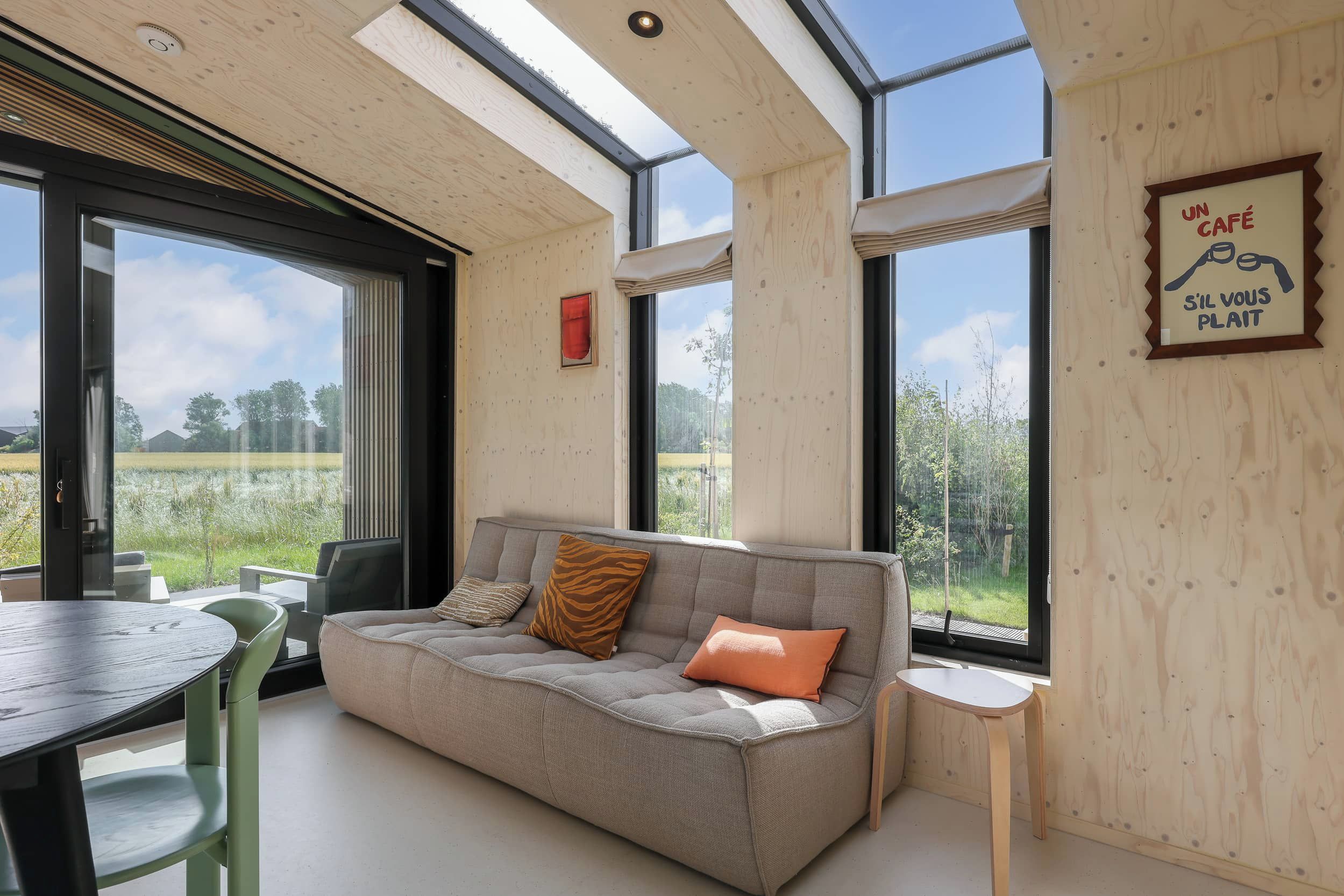 A modern interior with a sofa, a dining table, and large windows offering a view of a field.
