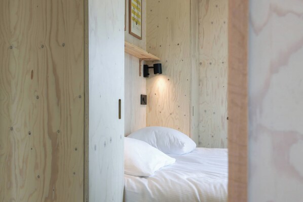 A room with a bed, a wall-mounted light, and a wooden door.