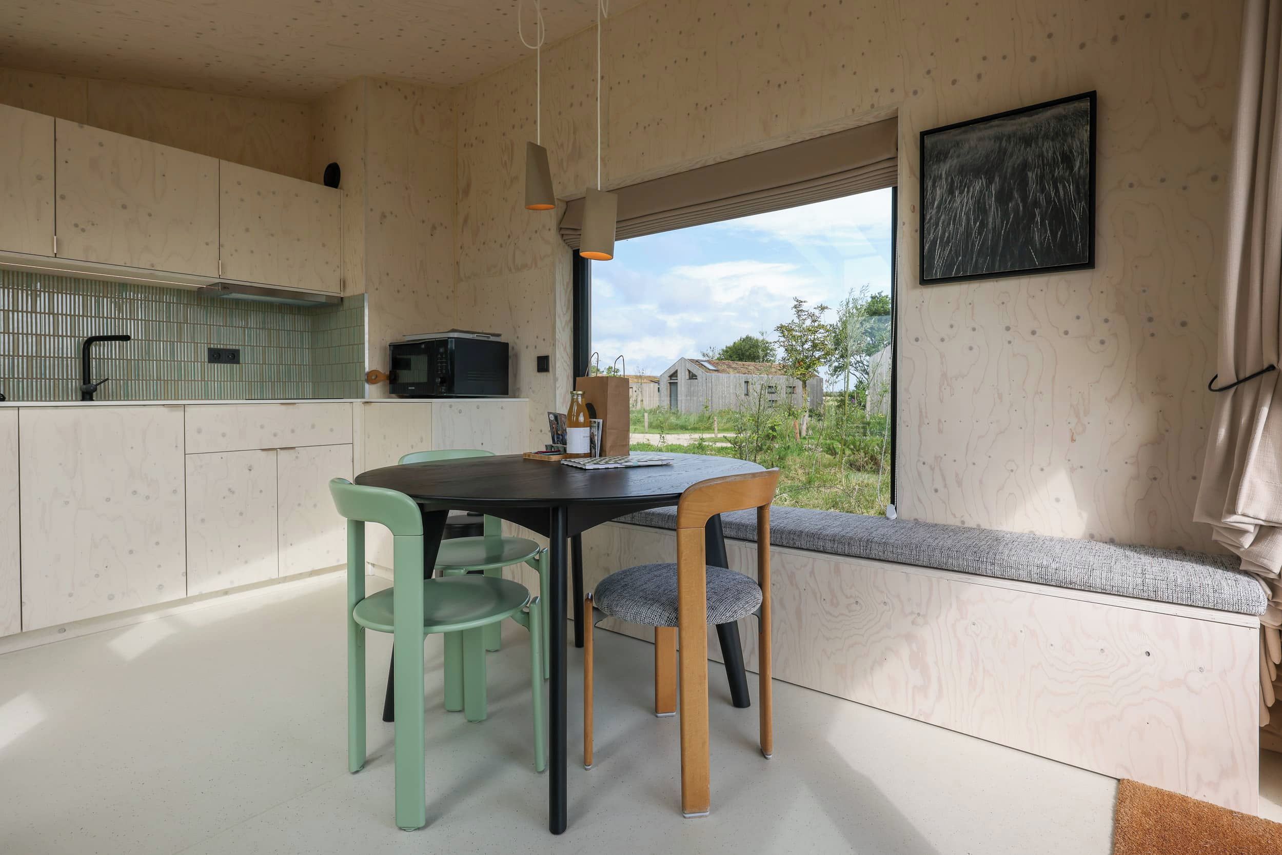 Une cuisine moderne avec un coin repas, des meubles en bois, une fenêtre avec vue et un banc agrémenté d’un coussin.