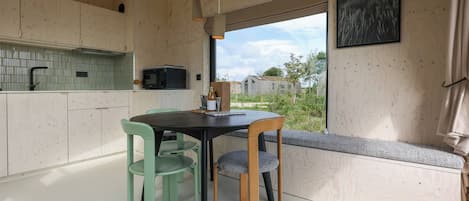 A modern kitchen with a dining area, wooden cabinets, a window with a view, and a bench with a cushion.