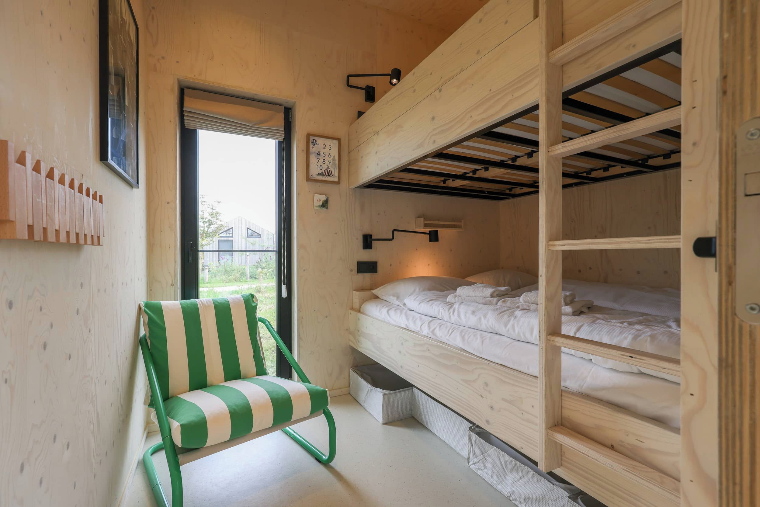 Une petite pièce avec un lit superposé, une chaise à rayures vertes et une fenêtre donnant sur un beau paysage.