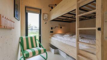Ein kleines Zimmer mit Etagenbett, einem grün gestreiften Sessel und einem Fenster mit Blick.