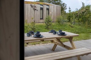 A wooden picnic table set with blue bowls and plates, a fork, and a spoon, with a wooden cabin in the background. - Single-storey tiny house for 4 in Westkapelle | Zeeuwse Liefde – Tiny House 9 (Westkapelle)