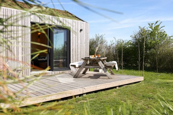 Una cabaña moderna de madera con terraza, puerta de cristal y mesa con sillas.