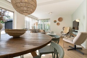 En moderne stue med et rundt træbord, en fletlampe og et hyggeligt opholdsområde med sofa og stole.