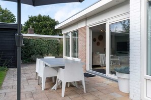 En patio med et bord, stole, en sort parasol og en skydedør, der fører til et rum indendørs.