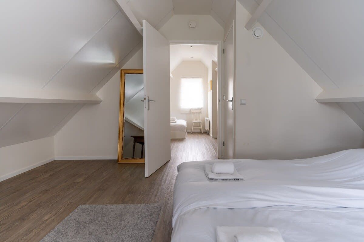 Un dormitorio con cama, una puerta que da a otra habitación y una escalera visible.