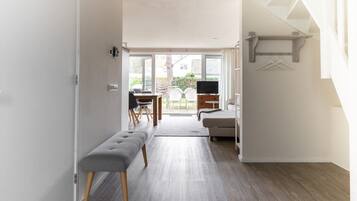 Un intérieur moderne avec un banc, un canapé et un téléviseur dans une pièce bien éclairée, offrant une vue sur l’extérieur.