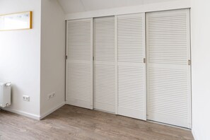 Una habitación con piso de madera, paredes blancas y un conjunto de armarios blancos con persianas.
