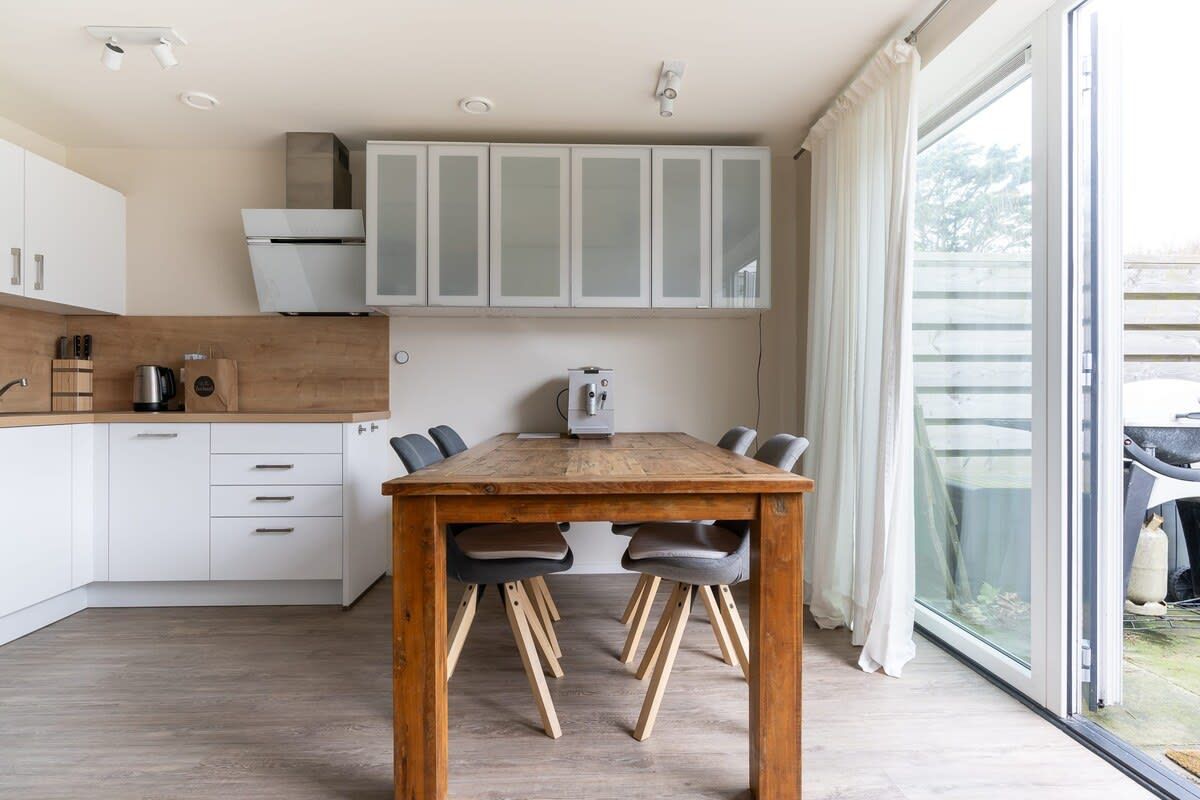 Una cocina moderna con armarios blancos, una mesa de madera y un ventanal corredero al exterior.
