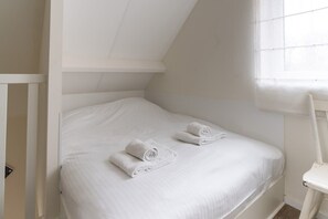 A single white bed with two neatly folded white towels, a white chair, and a window with blinds. - Holiday home near the sea in Domburg | Schelpweg 16A (Domburg)