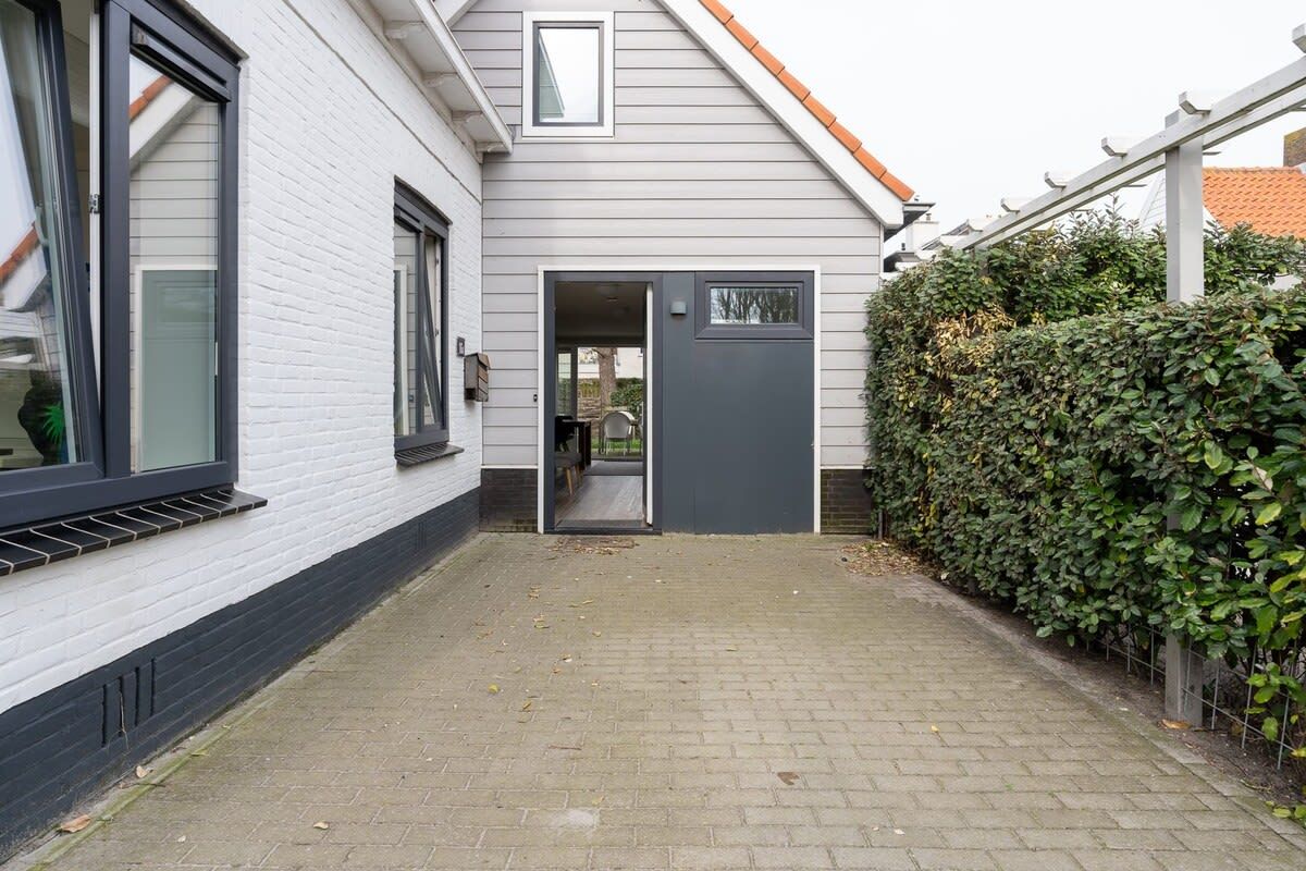 Ein Haus mit grauer Tür, weißer Fassade und einem gepflasterten Weg zum Eingang.