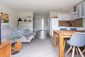 A modern living room with a sofa, coffee table, and dining table. There is a kitchen area with cabinets and a refrigerator. - Holiday home near the sea in Domburg | Schelpweg 16A (Domburg)