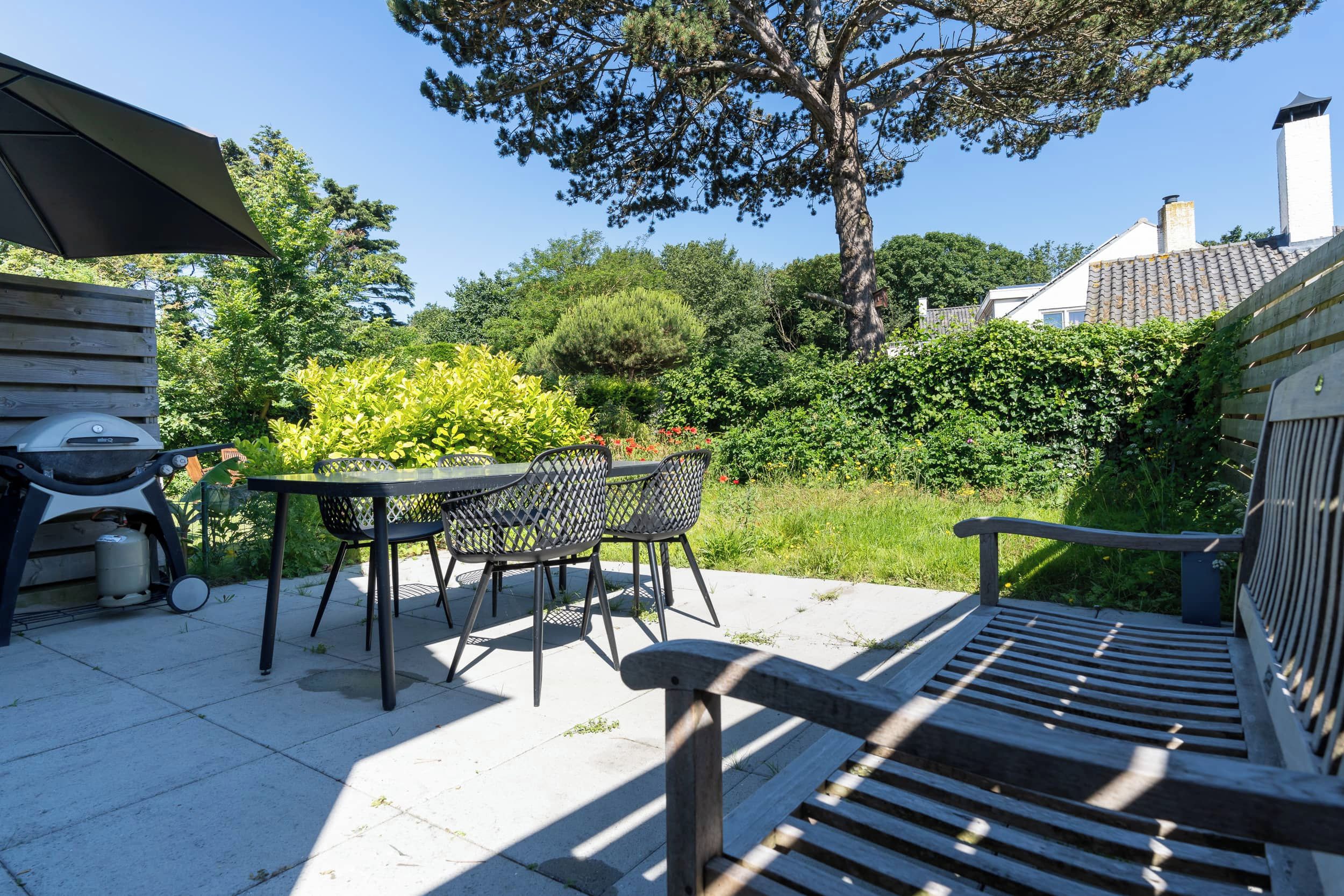 Eine Terrasse mit Tisch, Stühlen, einem Grill und einer Bank.