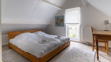 Un dormitorio con cama de madera, ventana con persianas, radiador, mesa con lámpara y un cuadro en la pared.