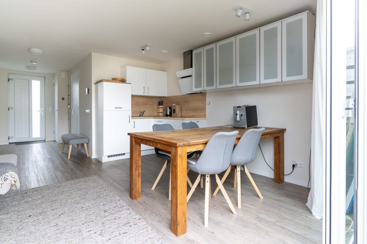 A modern kitchen with white cabinets, a wooden dining table, and grey chairs.