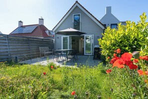 A residential property with a patio area, outdoor seating, and a garden with red flowers. - Holiday home near the sea in Domburg | Schelpweg 16A (Domburg)