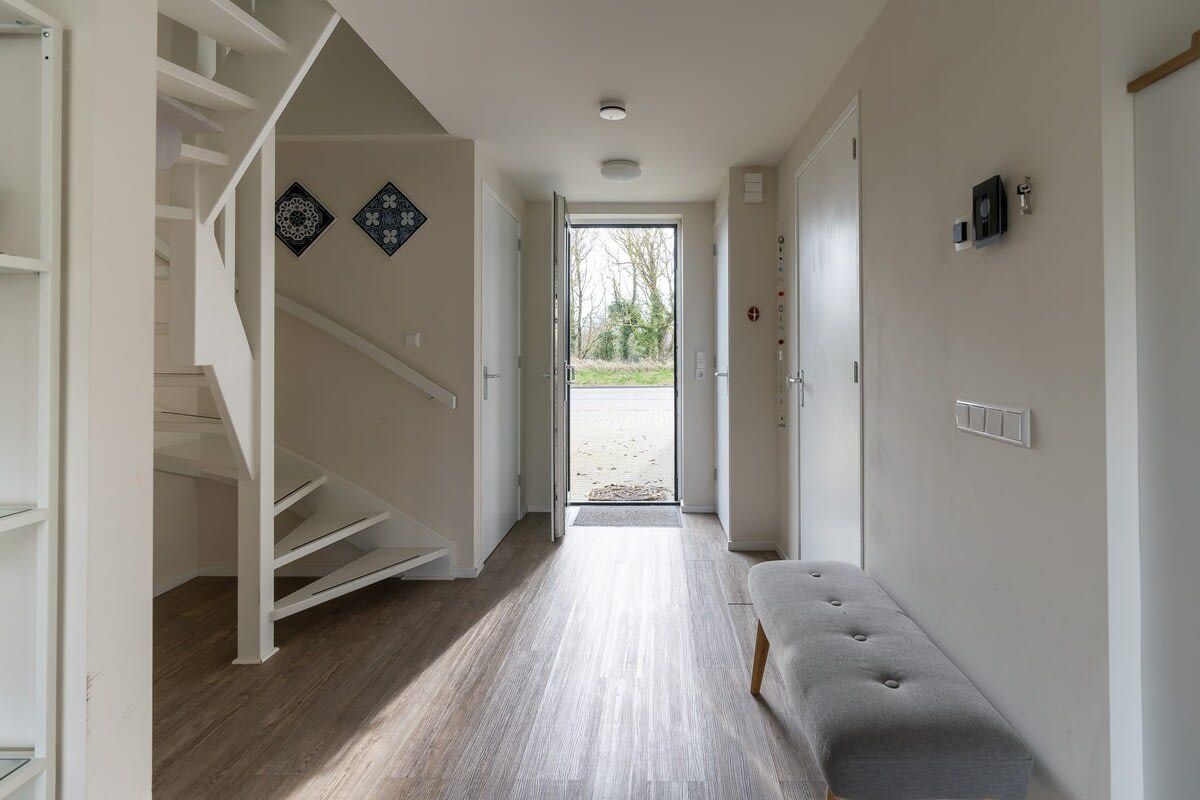A hallway with a staircase, a bench, and a door leading outside.