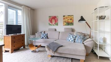 Ein Wohnzimmer mit einer Couch, einem Fernseher, einem Bücherregal und Kunstwerken an der Wand.