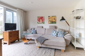 A living room with a sofa, a TV, a wooden cabinet, a bookshelf, and two wall-mounted flower paintings. - Holiday home near the sea in Domburg | Schelpweg 16A (Domburg)