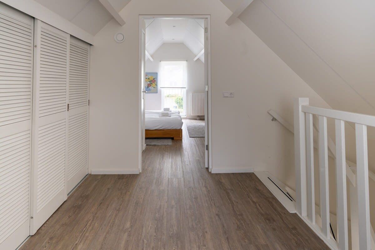 Ein schmaler Flur mit Holzboden führt zu einem Schlafzimmer mit Bett und Fenster.