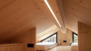 A wooden interior with a sloped ceiling, two beds, and a window.