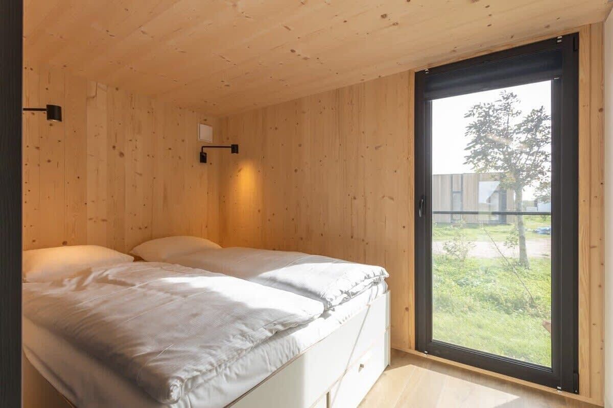 Un dormitorio con un ventanal grande, una cama y una lámpara fijada a la pared.