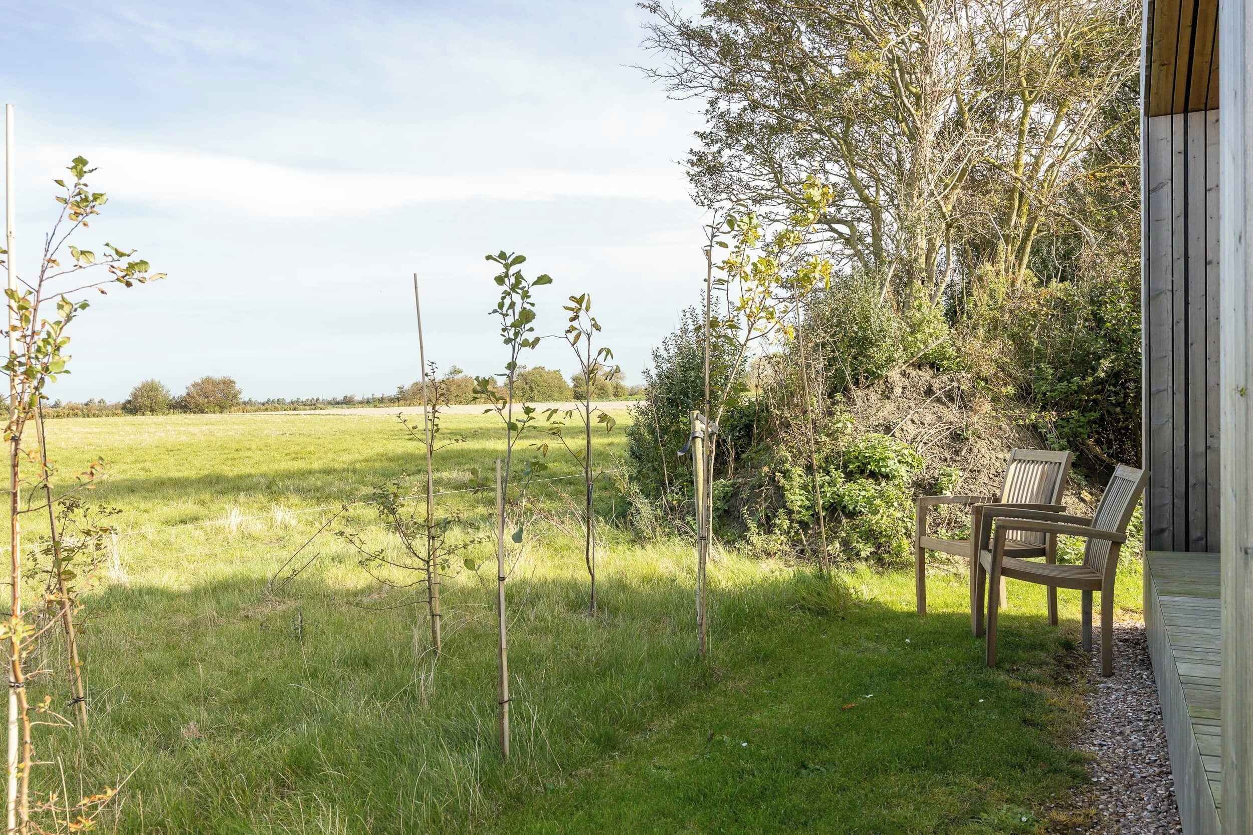 A wooden deck with two chairs, a grassy field, and trees in the background.